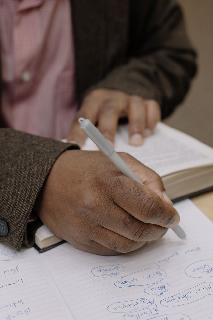person in pink and white gingham dress shirt holding pen writing on white paper